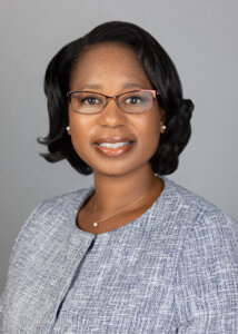 This is a headshot of Tiffany Donelson. She is wearing glasses and dressed in a gray jacket, against a gray background.