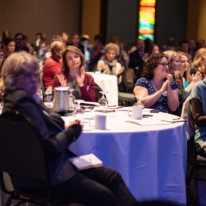 This is a picture of people sitting at a round table in a ballroom and applauding