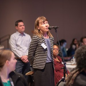 This is a photo of Elaine O'Keefe at a microphone asking a question during an event in a ballroom at the Connecticut Convention Center.