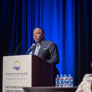 This is a photo of Dr. Kenneth Alleyne speaking at a podium that has the logo of the Connecticut Health Foundation on the front