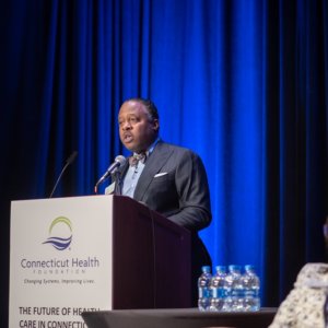 This is a photo of Dr. Kenneth Alleyne speaking at a podium that has the logo of the Connecticut Health Foundation on the front