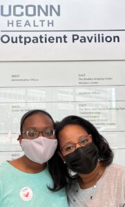 This is a photo of Tiffany Donelson and her daughter wearing masks and standing in front of a sign that says "UConn Health"