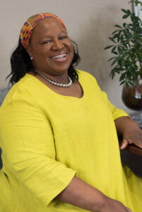 This is a portrait of Rev. Nancy Kingwood, president and executive director of the Greater Bridgeport Area Prevention Program. She is a Black woman who is wearing a yellow dress and a headband. 