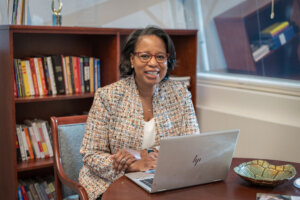 This is a photo of Tiffany Donelson sitting at a table with a laptop computer in front of her.